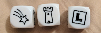 three dice showing a shooting star, a castle tower, and the letter L in a box